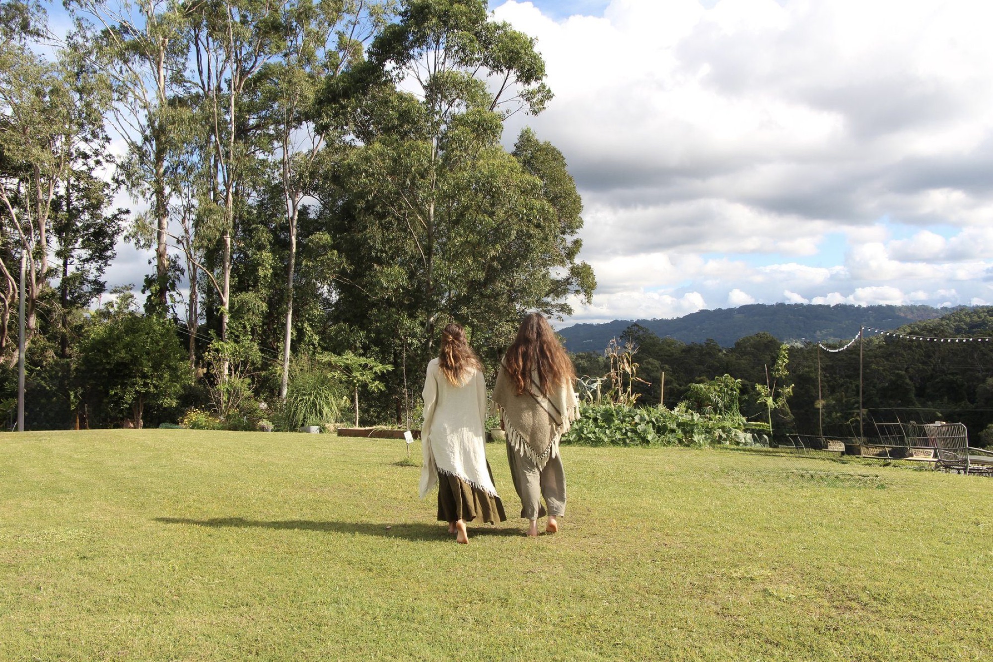 Two women walking together through a sunlit grassy field